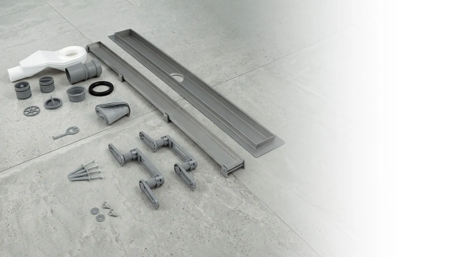 The Luxdrain STR set laid out on a stone floor, channel with grate, trap, levelling feet and fittings